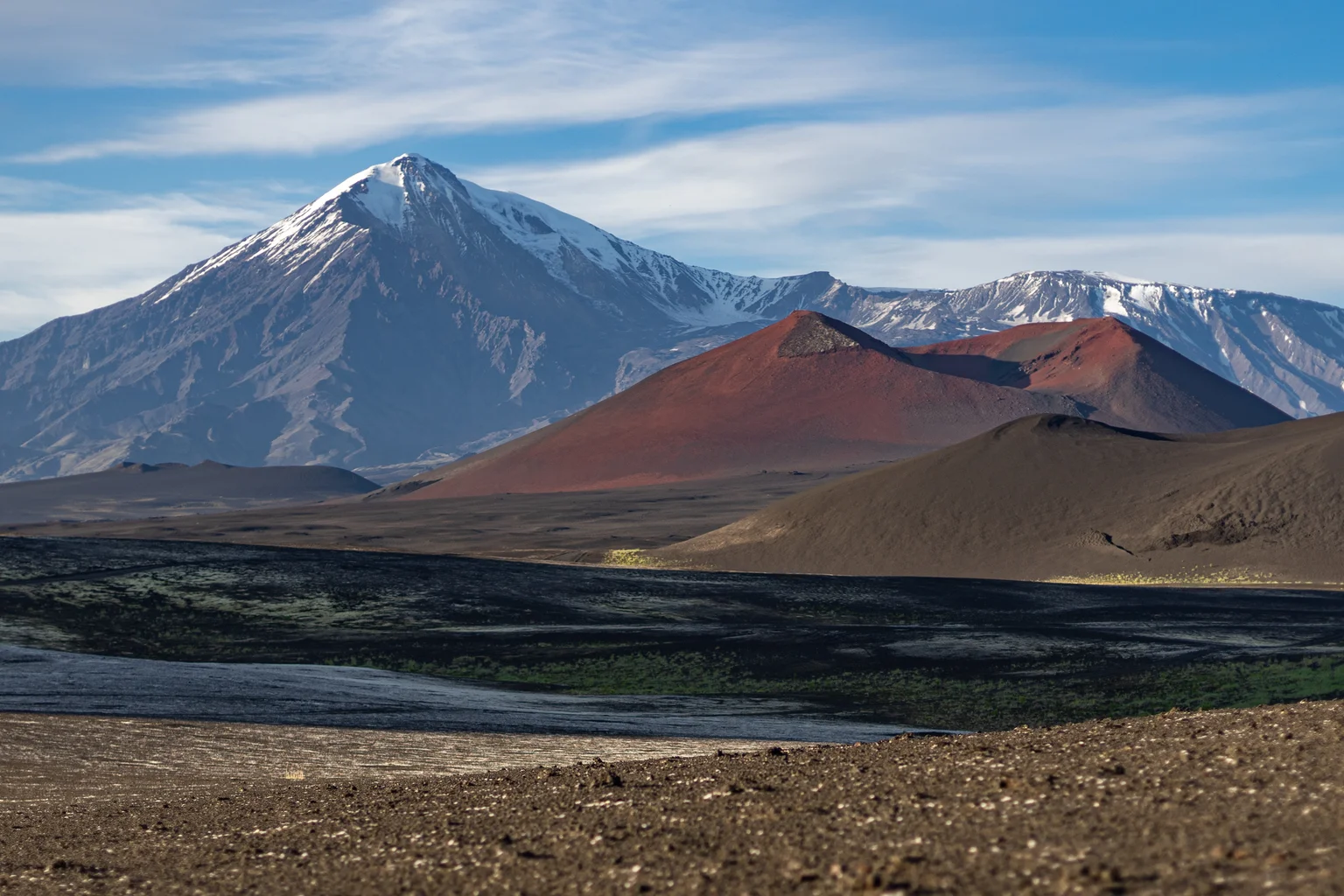 Cône volcanique fumant du Kamtchatka au crépuscule, toundra sauvage et ciel nuageux